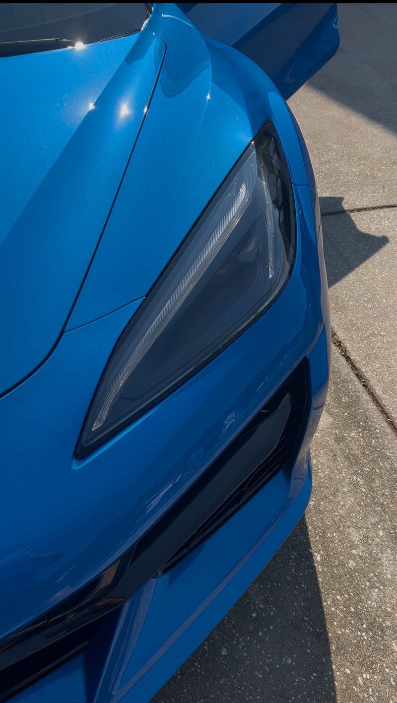 Close-up of a glossy blue Corvette headlight and hood after detailing